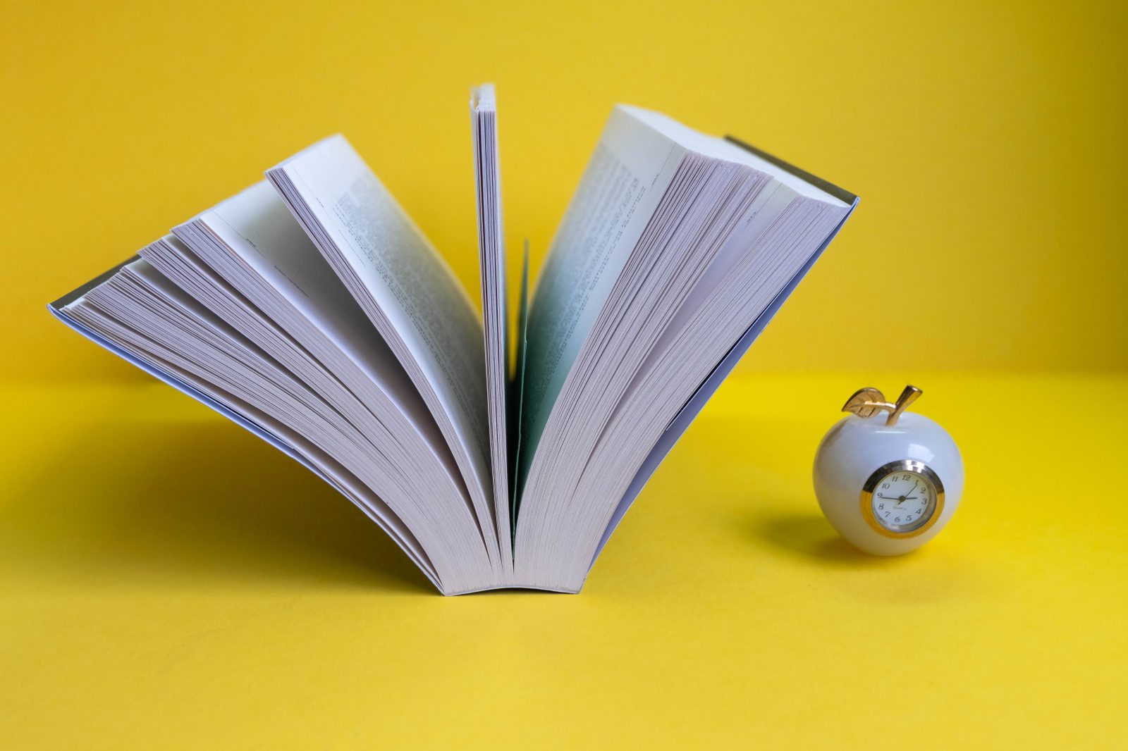 Open book with an apple and clock — education still life
